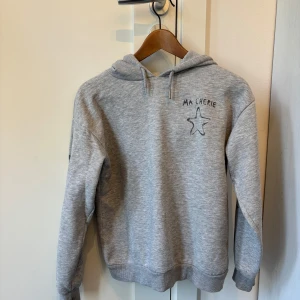 Grå hoodie från Gina Tricot - Grå hoodie från Gina Tricot med text 'MA CHERIE' och en stjärna på bröstet samt stjärnor på ärmarna. Mjuk insida och klassisk huva. 