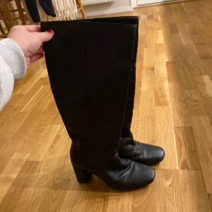 Svarta höga stövlar med klack - Säljer ett par svarta höga stövlar med bred klack och rund tå. Skorna är i skinn och går upp till knäet, skönaste bootsen jag haft på mig! Strl 39 