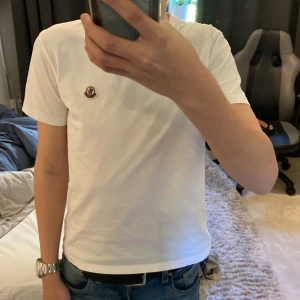 Vit t-shirt från Moncler äkta moncler !! - Säljer en klassisk vit t-shirt från Moncler med liten broderad logga på bröstet. T-shirten har rund hals och korta ärmar, perfekt för en clean och stilren look.