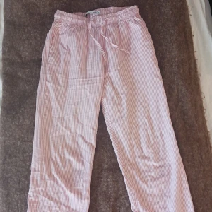 Rosa och vita randiga mjukisbyxor - Säljer ett par mjuka och sköna byxor med rosa och vita ränder. Byxorna har resår i midjan och dragsko för extra komfort. Perfekta för att chilla hemma eller som pyjamasbyxor. Byxorna är u storlek 150 men passar xxs/xs för lite kortare personer! Skriv bara vid frågor och svarar jag så snabbt jag kan!❤️ säljer dem för 40 kr