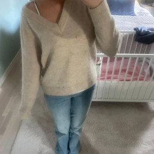 Beige stickad v-ringad tröja - Mysig beige stickad tröja med v-ringning och långa ärmar. Tröjan har en avslappnad passform och är perfekt för lager-på-lager. Enkel och stilren design som passar till mycket.