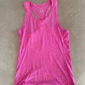 NIKE - Rosa träningslinne Dri-Fit - Säljer ett rosa träningslinne från Nike. Linnet har brottarrygg och är tillverkat i ett lätt och snabbtorkande material som passar perfekt för träning. Diskret Nike-logga på bröstet. Superskönt och snyggt linne!