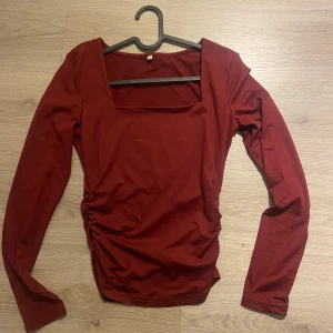 Vinröd långärmad topp med fyrkantig ringning - Säljer en vinröd långärmad topp med snygg fyrkantig ringning och lätt rynkade detaljer på sidan.