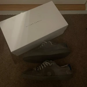 Grå sneakers från Oliver Cabell - Säljer ett par stilrena grå sneakers från Oliver Cabell med vita skosnören och diskret logga på sidan. Skorna har rund tå och platt sula, perfekta för en avslappnad look. Levereras med originalkartong.