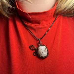 Handgjort halsband med vit sten och metalltråd - Unikt halsband med en stor vit sten infattad i svart och kopparfärgad metalltråd, formad som ett bär. Hängs i ett svart snöre. Perfekt för dig som gillar personliga och kreativa smycken.