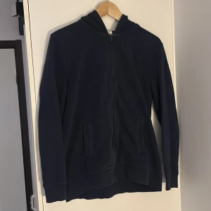 Mörkblå hoodie från H&M BASIC - Mörkblå hoodie från H&M BASIC med dragkedja framtill och två fickor. Klassisk modell med huva och långa ärmar, perfekt för en avslappnad stil.