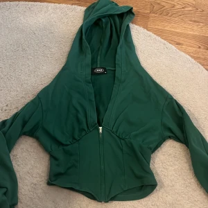 Tröja - Säljer en grön croppad hoodie från ODDI med dragkedja framtill. Tröjan har långa ärmar, stor huva och markerad midja för en snygg passform. Perfekt för dig som vill ha en trendig och bekväm look.