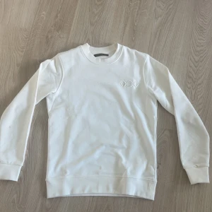 Vit sweatshirt från Louis Vuitton - Säljer en stilren vit sweatshirt från Louis Vuitton med broderad LV-logga på ryggen och diskret broderad detalj framtill. storlek s och den är true to size.priset är inte hugger i sten .