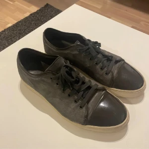 Grå sneakers från Lanvin med svarta detaljer - Säljer ett par grå sneakers från Lanvin med svarta skinn-detaljer på tån och snörning. Skorna har vit sula och en stilren design som passar till många outfits.