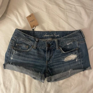 Low waist jeansshorts från American Eagle - Super snygga blå jeansshorts från American Eagle med slitna detaljer och fransig kant. Klassisk femficksmodell med låg midja och uppvikta benslut. Köpt på Sellpy men var tyvär för små för mig.