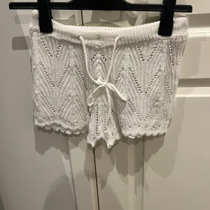 Vita stickade shorts med knytband - Säljer ett par vita stickade shorts med snyggt mönster och knytband i midjan. Shortsen har en söt, vågig kant nertill och är perfekta för sommaren. Materialet är 100% polyester och de har en normal passform. Aldrig använda & pris kan diskuteras