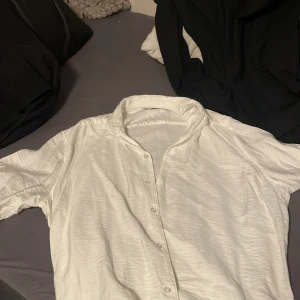 Vit skjorta från Smog - Säljer en klassisk vit skjorta från Smog i storlek L. Skjortan har krage, knäppning framtill och är tillverkad i ett lätt, strukturerat tyg. Perfekt för en clean och stilren look.