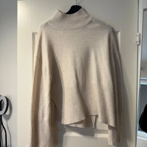 Beige stickad polotröja - Säljer en oversized beige stickad polotröja med bred ribbstickning nedtill och på ärmsluten. Tröjan har hög polokrage och långa ärmar, perfekt för kyliga dagar. Supermjuk och skön att bära.