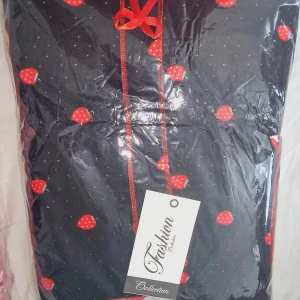 Söt klänning med jordgubbsmönster och rosett - Klänning med jordgubbsmönster och små prickar, dekorerad med en röd rosett framtill. Finns i svart, rosa och vit med kontrasterande kantband. Perfekt för dig som gillar gulliga detaljer och lekfull stil.