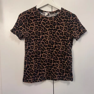 Leopardmönstrad t-shirt - T-shirt med leopardmönster i bruna och svarta toner. Klassisk passform med rund halsringning och korta ärmar. 