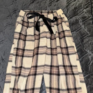 Pyjamasbyxor  - Säljer ett par rutiga pyjamasbyxor i beige, svart och brunt med elastisk midja och svart knytband. Byxorna har en avslappnad passform och är perfekta för chill dagar hemma. Använda ett par gånger men är i jättebra skick!! Passar båda tjejer och killar beroende på hur man vill att de sitter.