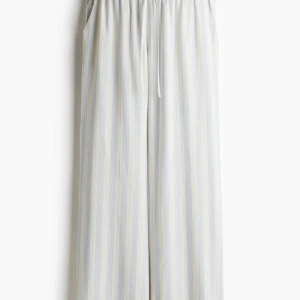 Randiga vida linnebyxor med dragsko - Luftiga byxor med ljusblå och vita ränder, vida ben och elastisk midja med dragsko. Perfekta för en avslappnad stil och passar bra till t-shirt eller skjorta. Byxorna har aldrig används och säljs för att de är för korta för mig!