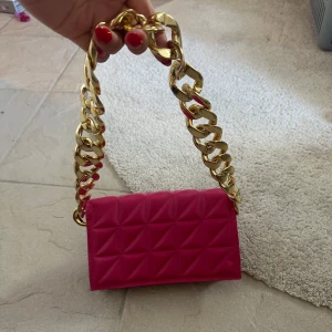 Rosa quiltad mini axelväska med guldkedja - Säljer en superfin rosa mini axelväska med quiltat mönster och en chunky guldfärgad kedja som handtag. Perfekt för att lyfta vilken outfit som helst! Väskan har magnetlås och plats för det viktigaste.