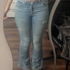 Blå bootcut jeans - Säljer ett par klassiska blå bootcut jeans med lätt slitning på låret. Jeansen har normal passform och är tillverkade i denim. Perfekta för dig som gillar en tidlös stil med lite utsvängda ben. Jag säljer dessa på grund av att de är för korta för mig. Storleken är 28 men de passar mig som brukar variera mellan xs och s!!!