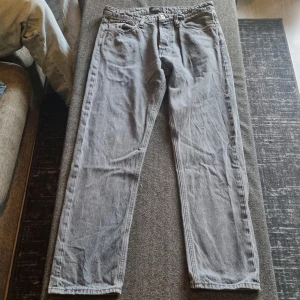 Grå jeans från Jack & Jones - Säljer ett par grå jeans från Jack & Jones i klassisk rak modell. Byxorna har fem fickor, bälteshällor och stängs med dragkedja och knapp. Perfekta för en avslappnad stil.