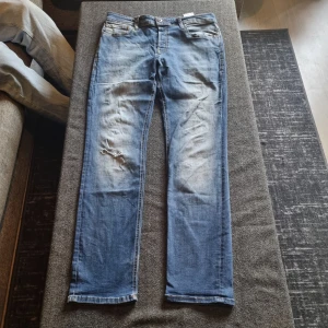 Blå slim straight jeans - Säljer ett par blå jeans med slim straight passform. Byxorna har klassisk femficksdesign, dragkedja och knapp i midjan samt slitningar på ena benet för en cool look. Storlek W32 L32. PRIS:150KR