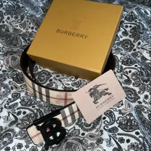 Burberry bälte  - Säljer ett Burberry bälte med det ikoniska beigea rutmönstret och ett stort svart 'B'-spänne. Bältet har detaljer i svart, rött och vitt och är tillverkat i skinn. Perfekt accessoar för att lyfta din outfit. Skick 10/10✅