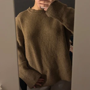 Beige stickad tröja med rund hals - Mysig beige stickad tröja med rund hals och långa ärmar. Tröjan har en avslappnad passform och breda ribbade muddar vid ärmslut och nederkant. Perfekt för kyliga dagar.