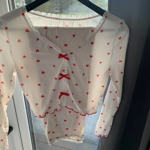 Vit pyjamas med röda hjärtan och rosetter - Supersöt vit  pyjamas med röda hjärtan och röda rosetter framtill. . Perfekt för dig som gillar gulliga detaljer!