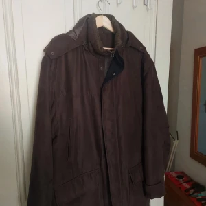 Brun parkajacka från London Fog - Säljer en brun parkajacka från London Fog i storlek L. Jackan har huva, dragkedja och knappar framtill samt flera fickor. Fodrad insida för extra värme och klassisk design som passar till många tillfällen.