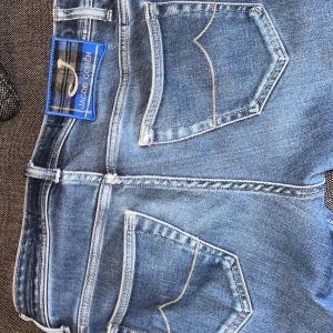 Blå jeans från Jacob Cohen - Säljer ett par klassiska blå jeans från Jacob Cohen med snygga kontrastsömmar och femficksmodell. Byxorna har gylf med knappar och detaljer i guld, samt en patch med varumärket bak. 
