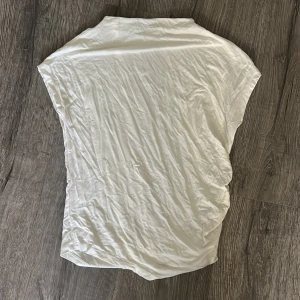 Vit t-shirt från lager 157 - En vit T-shirt med mjukt tyg som man både kan klä upp och klä ner. Perfekt att ha tröja. Den har på sidan av tröjan en detalj (lite Scrunch). Den är även lite kortare i axeln en vad vanliga t-shirts är sedan har den även en liten högre krage men inte polo. Denna T-shirt är i storlek S 