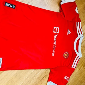 Manchester United fotbollströja Ronaldo 7 - Säljer en röd Manchester United fotbollströja från Adidas med TeamViewer sponsortryck och klubbmärke på bröstet. Tröjan har vita detaljer, korta ärmar och Ronaldo 7-tryck på ryggen. Perfekt för fans av laget!