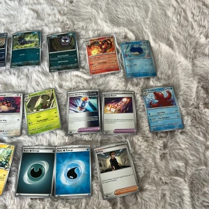 Samling Pokémonkort - Säljer en blandad samling Pokémonkort med både vanliga och holografiska kort. Innehåller flera olika Pokémon, energikort och tränarkort. Flera kort har färgstarka illustrationer och vissa är V-kort med högre HP. Perfekt för samlare eller Pokémon-fans som vill utöka sin samling.