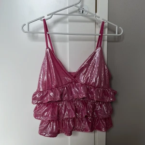  Rosa volangtopp - Säljer en glittrig rosa topp med flera lager volanger. Toppen har en snygg v-ringning framtill. Perfekt för dig om du ska ut på fest och väldigt snyggt för konsärer. Jag säljer den föratt jag skulle på fest men de blev ändå ingen fest. Och jag köpte toppen bara för festen. Så den är inte använd❤️❤️