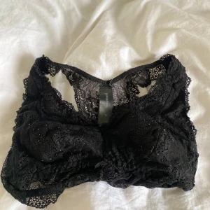 Svart spets bralette från Sassy Inani - Svart bralette från Sassy Inani i storlek M. Toppen är tillverkad i spets med fina blommiga detaljer och har en mjuk, stretchig passform utan byglar. Perfekt för en trendig och bekväm look.