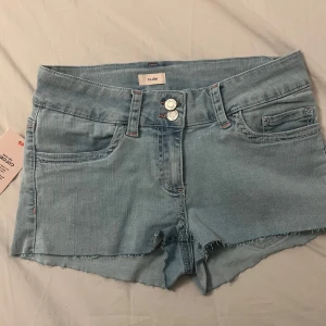 Stitch Jeans Shorts  - Snygga ljusblå jeansshorts med rosa detaljer och dubbla knappar framtill. 