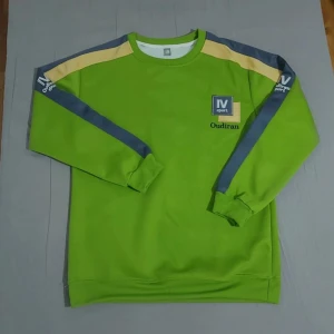 Grön sweatshirt från IV Sport - Cool grön sweatshirt från IV Sport med broderad logga och texten 'Oudirán' på bröstet. Tröjan har långa ärmar med grå och beige detaljer längs axlar och ärmar. Perfekt för en sportig look.