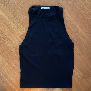 Svart ärmlös linnetopp från Zara - Säljer en svart, stilren ärmlös linnetopp från Zara. Toppen har rund halsringning och är tillverkad i ett mjukt, stretchigt material som sitter skönt mot kroppen. Perfekt att matcha med jeans eller kjol.