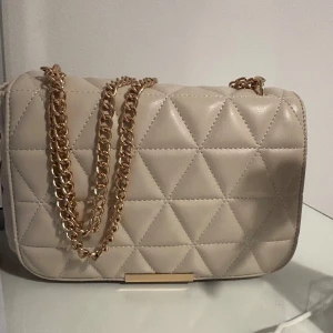 Beige quiltad axelväska med guldkedja - Säljer en beige axelväska från Glitter! Har använt den en gång, köptes för 399 men säljes för 280kr!🤍🤍🤍