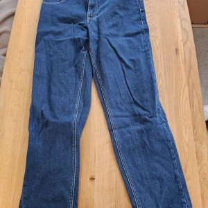 Blå jeansbyxor från ASOS DESIGN - Säljer ett par klassiska blå jeansbyxor från ASOS DESIGN. Byxorna har raka ben, normal passform och tydliga kontrastsömmar. Utrustade med fem fickor och normal midja. Perfekta för dig som gillar en enkel och tidlös stil.