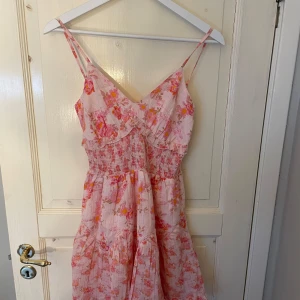 Blommig rosa klänning  - Supersöt rosa klänning med blommigt mönster.. Köpt från Asos. smala axelband och snörning i ryggen. Perfekt för sommarens alla tillfällen! Helt ny och aldrig använd
