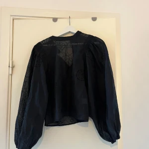 Svart blus  - Svart blus med blommigt mönster. Knappfästet är av i ryggen men går lätt att lösa 