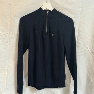 Svart ribbad tröja med dragkedja från Gant - Säljer en svart ribbad tröja från Gant med halv dragkedja framtill och broderad logga på bröstet. 158/164 (13-14 år)