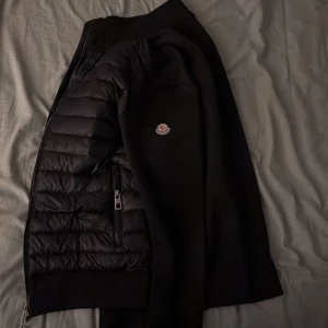 Svart pufferjacka från Moncler - Perfekt för sommaren Säljer en svart pufferjacka från Moncler med quiltade partier framtill och släta ärmar. Jackan har dragkedja, Moncler-logga på ärmen och en snygg, sportig look. Perfekt för dig som vill ha något stilrent och bekvämt. (Har L och passar perfekt) 