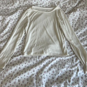 Vit långärmad ribbad topp - Säljer en enkel och stilren vit långärmad topp med diskret ribbat mönster. Perfekt att matcha med jeans eller kjol för en clean look. Mjuk och skön mot huden.