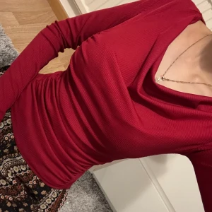 Röd ribbad långärmad topp med drapering - Säljer en snygg röd långärmad topp med ribbad struktur och draperad detalj framtill. Toppen har en vid, något v-ringad halsringning och sitter tight. Perfekt att styla med både jeans och kjol! Storlek xs/s 