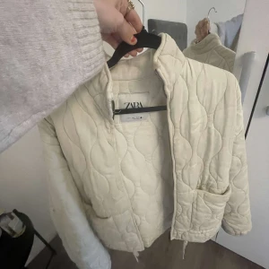 Beige zara jacka  - Säljer en beige quiltad jacka med dragkedja och hög krage. Köptes för 849kr.Jackan har lång ärm och dragsko i nederkant för justerbar passform. Perfekt för kyliga dagar och enkel att styla till olika outfits.