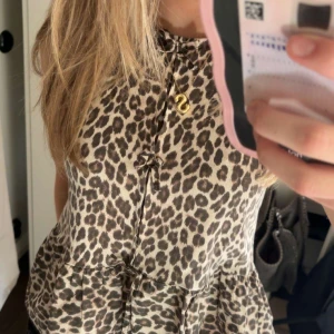 Leopardmönstrad blus med knyt - Säljer en snygg blus med leopardmönster och knyt framtill. Blusen har en lös passform och är ärmlös, perfekt för att sticka ut lite extra. Passar till både jeans och kjol. Stolek 164 cm
