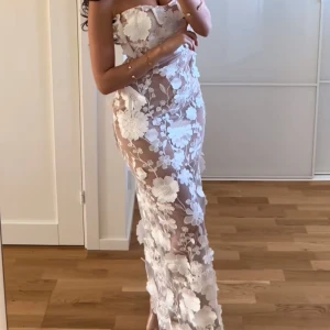 Vit axelbandslös långklänning med blommig spets - Säljer en elegant axelbandslös långklänning i vit spets med stora blommiga. Klänningen är figurnära och har transparenta partier samt dragkedja bak. Aldrig använd!! Storlek M mycket mindre i storlek. Passade på min syster som har XS. Köpte för 1,3 med frakt, säljer för 600. 