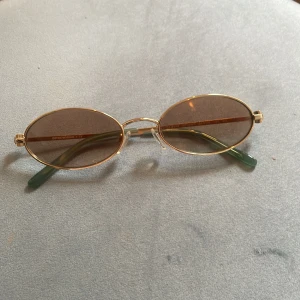 Armani solglasögon  - Snygga ovala solglasögon från Emporio Armani med tunna guldfärgade metallbågar och bruna glas. Skalmarna är gröna och har märkets logga på sidan. Vintage-stil. Nypris 1800 kronor. Storlek 54-19 med nässadlar så går att justera. 